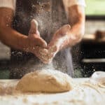 Chef's hands spraying flour over the dough